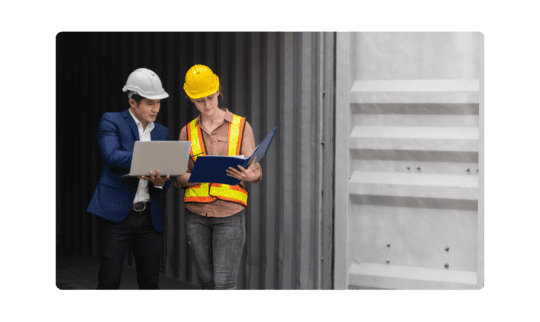 Man and woman wearing construction helmet looking at computer.