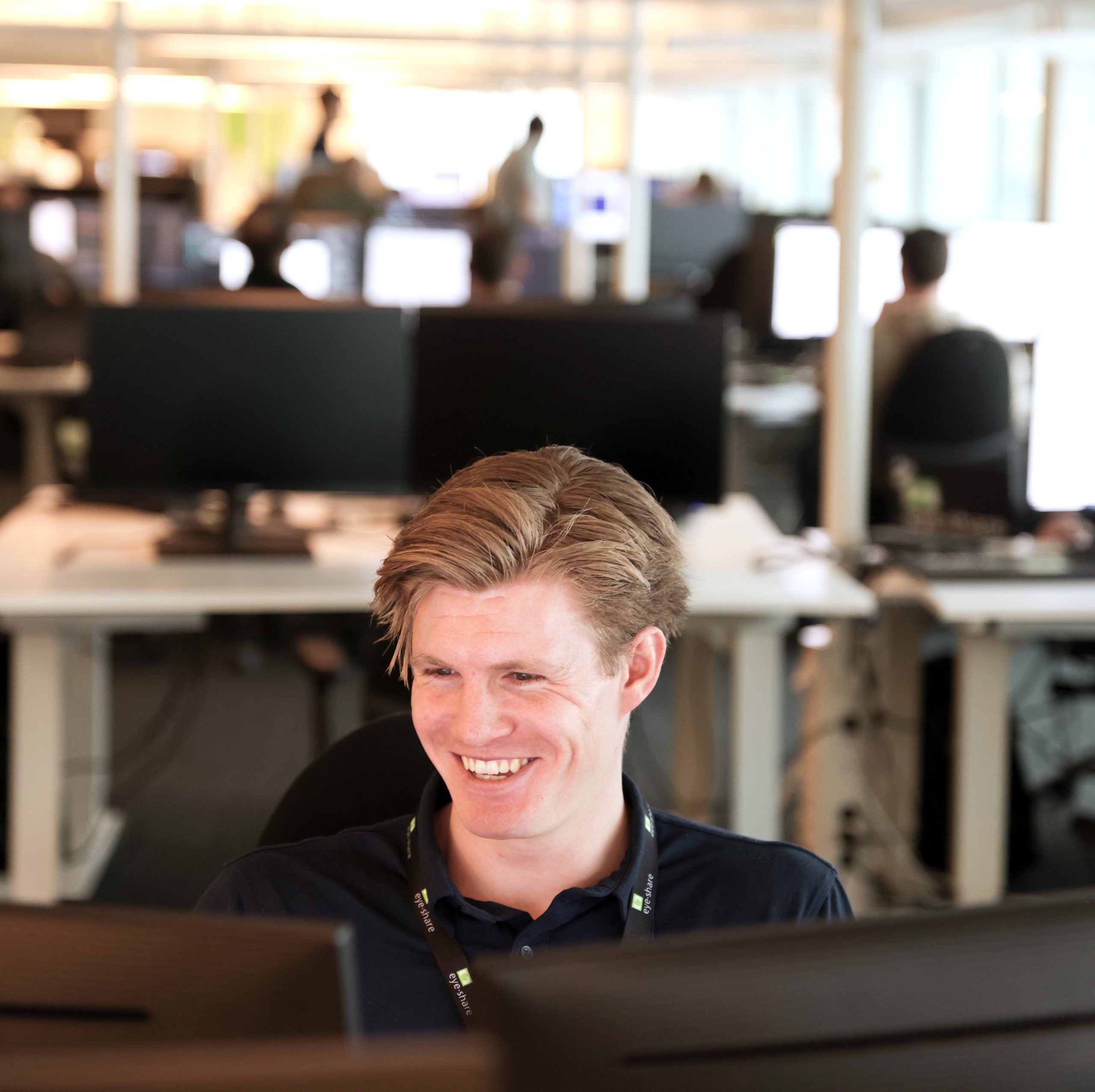 Eye-share employee, William Skaar, smiling in front of computer in office environment