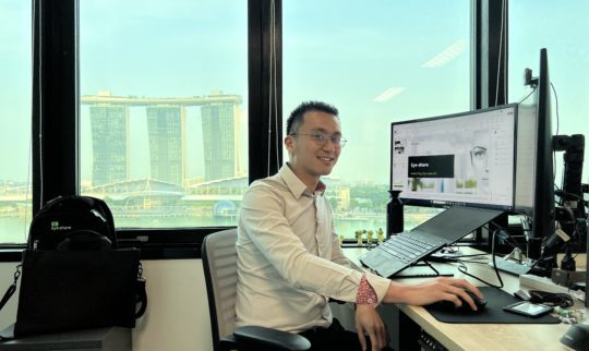 Eye-share employee sitting in office with view over Marina Bay, Singapore.